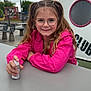 Joy a rejoint le concours — aidez-le/la à gagner de superbes lots ! child, girl, glasses, pigtails, pink_jacket, smiling, outdoor, table, hand, spray_bottle, playground, structure, cloudy_sky, bench, urban, person, hair, casual, daytime, happy