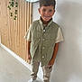 child, boy, smile, standing, indoor, casual_clothing, puffer_vest, beige_pants, white_sneakers, bracelet, wooden_wall, mirror, green_plant, modern_interior, happy, portrait, fashion, short_hair, light, floor