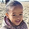 beach, child, close_up, coat, earring, girl, hair_bun, happy, horizon, jacket, ocean, person_in_background, polka_dots, portrait, sand, smile, sunlight, teeth, walking, waves