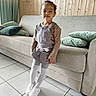 child, cozy, curtains, furniture, girl, green_pillows, happy, indoors, living_room, overalls, painting, portrait, smiling, sneakers, sofa, standing, striped_tights, tiled_floor, wall_lamp, wood_paneling