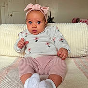 Audriana is registered to the contest to win money with this photo: baby, child, infant, headband, pink, sweater, knitted_pants, white_socks, couch, blanket, indoor, portrait, cute, seated, clothing, person, face, expression, cozy, home