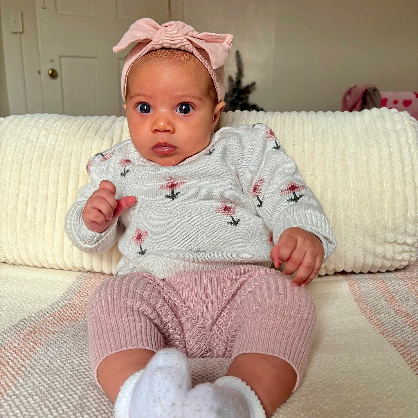 Audriana is registered to the contest to win money with this photo: baby, child, infant, headband, pink, sweater, knitted_pants, white_socks, couch, blanket, indoor, portrait, cute, seated, clothing, person, face, expression, cozy, home