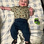 baby, child, smiling, blanket, shirt, pants, sandals, indoor, happy, cute, infant, blue, green, footwear, clothing, face, person, lying_down, patterned, comfortable