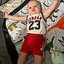 Michal is registered to the contest to win money with this photo: baby, child, infant, sporty, jordan, red_shorts, white_tank_top, dinosaur_blanket, plush_toy, lying_down, arms_outstretched, cute, indoors, soft_toy, colorful, happy, face, sock, footwear, crib