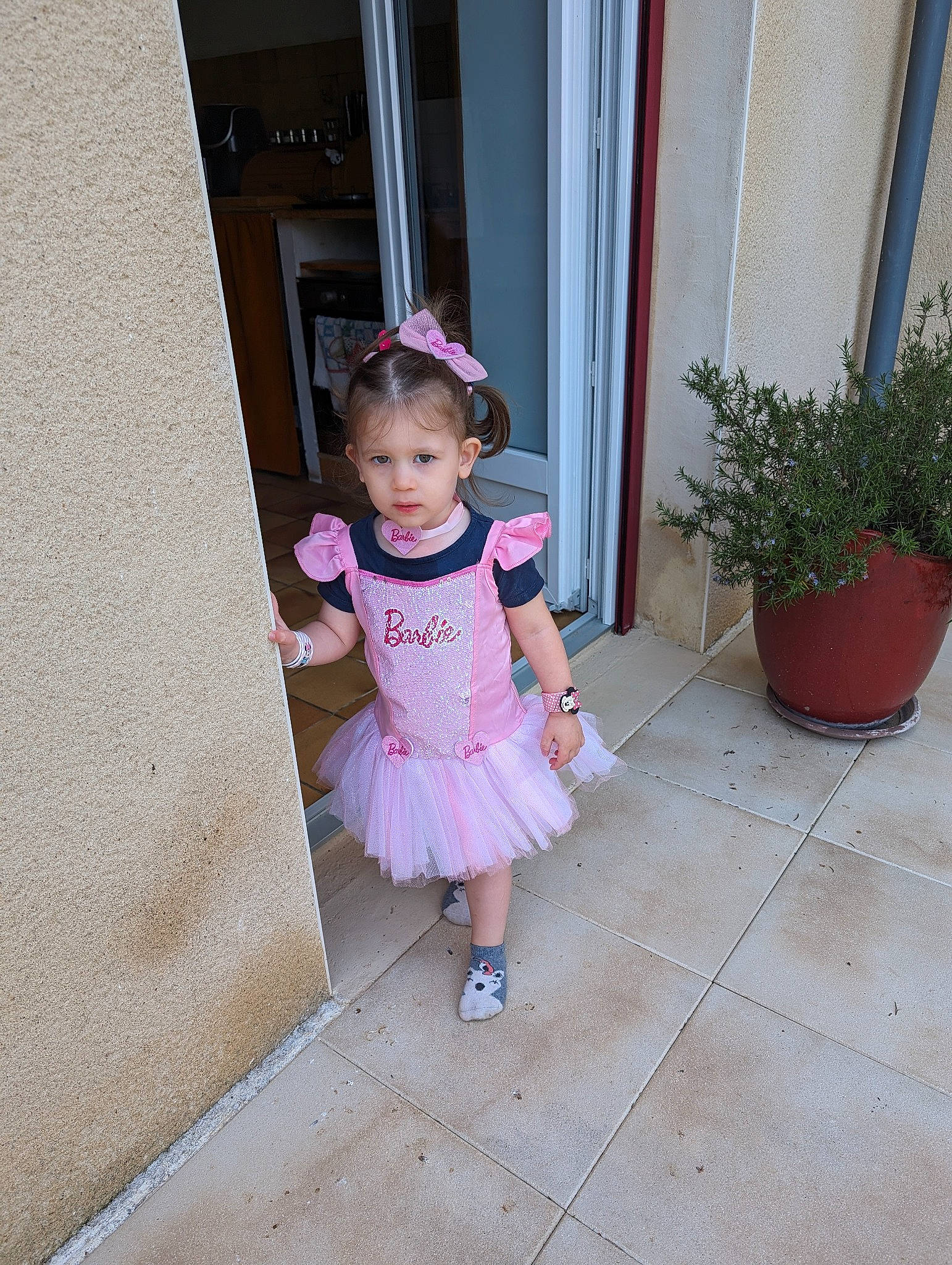 Maëlia participe au concours pour gagner de l'argent avec cette photo : baby, baby_toddler_clothing, child, concrete, day_dress, door, face, flooring, flowerpot, fun, houseplant, human_leg, magenta, pattern, person, pink, plant, purple, sandal, toddler