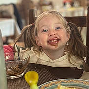 Aurore participe au concours pour gagner de l'argent avec cette photo : child, toddler, pigtails, chocolate, messy_face, smile, dining_table, bowl, plate, spoon, slice_of_cake, bread, cup, high_depth_of_field, background_people, blurry, hoodie, happy, seat, portrait