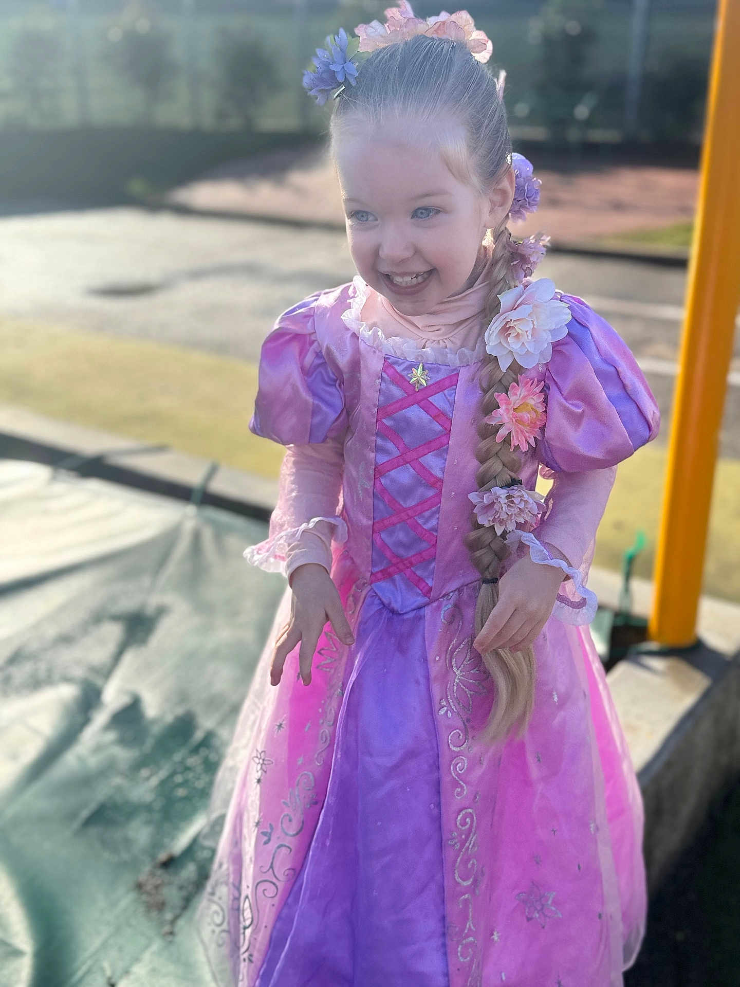 Aurore participe au concours pour gagner de l'argent avec cette photo : child, girl, princess, costume, pink_dress, purple_dress, braid, flowers, smile, playground, outdoors, sunlight, portrait, happy, candid, young_child, hair_accessory, fairy_tale, shallow_depth_of_field, daylight