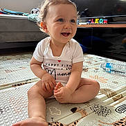 Leo joined the competition — help win amazing prizes! baby, child, smiling, sitting, curly_hair, indoor, playmat, foot, hand, white_onesie, toy, wooden_blocks, television, couch, water_bottle, window, natural_light, floor_mat, living_room, happy