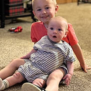 Dexton is registered to the contest to win money with this photo: child, baby, sitting, carpet, indoor, smiling, curious, clothing, footwear, person, home, floor, toy, background, happy, expression, blond_hair, striped_clothes, casual, young