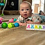 Dexton joined the competition — help win amazing prizes! baby, child, indoor, toy, colorful, plastic_eggs, curious, face, smiling, carpet, clothing, sign, playful, blue_eyes, cute, portrait, lying_down, home, expression, infant
