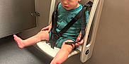 Dexton is registered to the contest to win money with this photo: toddler, child, baby, safety_seat, wall_mounted, straps, barefoot, curious, indoor, floor, hair, clothing, onesie, seat, neutral_colors, expression, small_feet, plastic, room, childcare