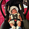baby, infant, car_seat, white_clothing, socks, hat, black, red_blanket, indoor, child, smiling, cute, newborn, safety_harness, seat, portrait, resting, looking, person, baby_boy