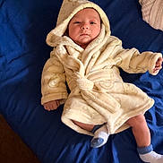 Moses is registered to the contest to win money with this photo: baby, infant, robe, hood, bed, blanket, blue_bedspread, sock, lying_down, indoor, person, clothing, cute, soft_texture, sleepwear, newborn, calm, portrait, child, babywear