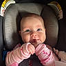 baby, child, car_seat, pink_clothing, hands, fingers, blue_eyes, face, infant, cute, rosy_cheeks, sitting, seatbelt, soft_lighting, indoor, closeup, portrait, playful, cozy, smiling