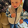 blond_hair, boy, chair, child, clothing, curious, eyes, face, indoors, jacket, jeans, laundry, living_room, portrait, shoes, slipper, smiling, standing, toddler, vest