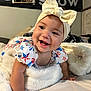 baby, smiling, headband, bow, infant, blanket, bed, clothing, star_pattern, happy, face, child, indoors, cute, person, portrait, skin, hand, fabric, room