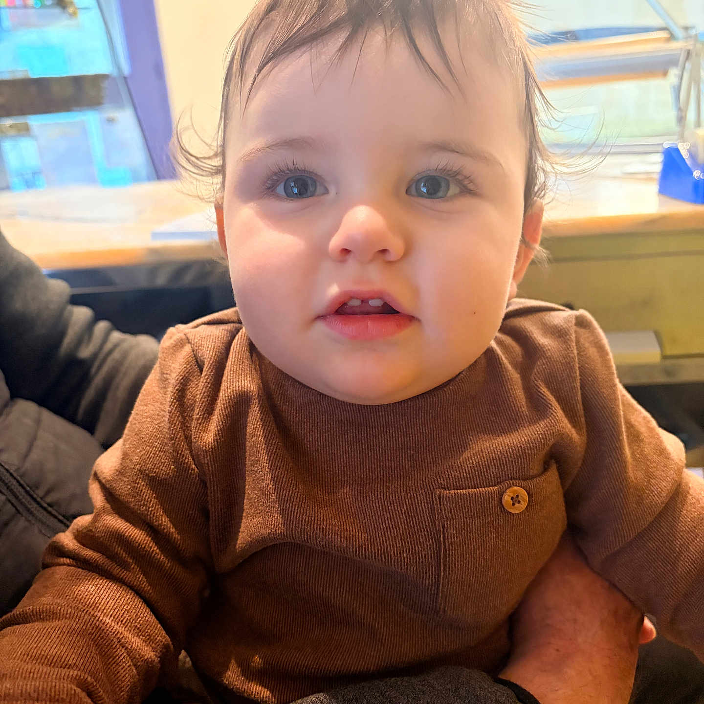 Adan participe au concours pour gagner de l'argent avec cette photo : adult_arm, baby, blue_eyes, brown_sweater, casual_clothing, child, close_up, cute, expression, face, hair, hand, indoor, person, portrait, skin, soft_lighting, toddler, warm_colors, young_child