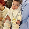 adult, baby, blue_suit, child, church, eyes, face, hand, holding, indoor, infant, person, pillar, portrait, red_hair, sash, special_event, suit, white_clothing, wooden_chair