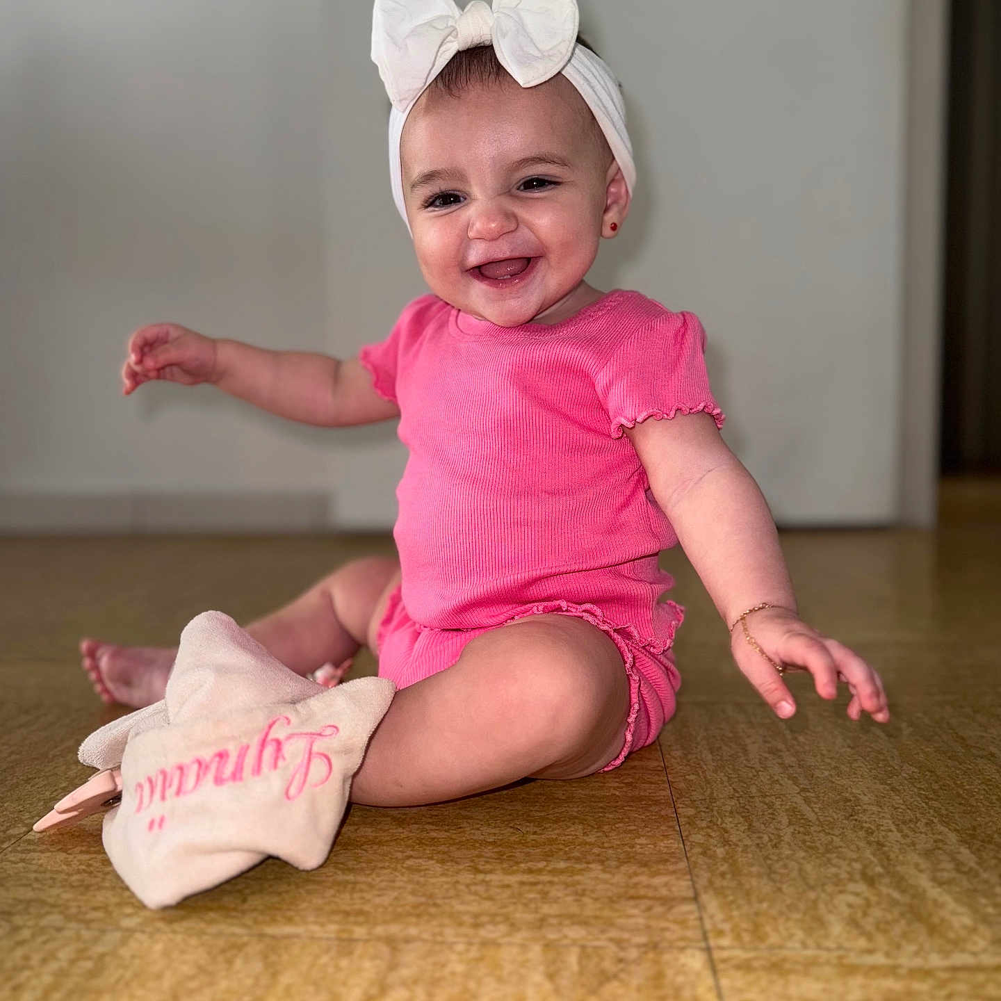 Lynaïa a rejoint le concours — aidez-le/la à gagner de superbes lots ! accessory, baby, bow, child, cute, door, earrings, floor, happy, headband, indoor, infant, jewelry, person, pink_clothing, plush_toy, portrait, sitting, smiling, wooden_floor
