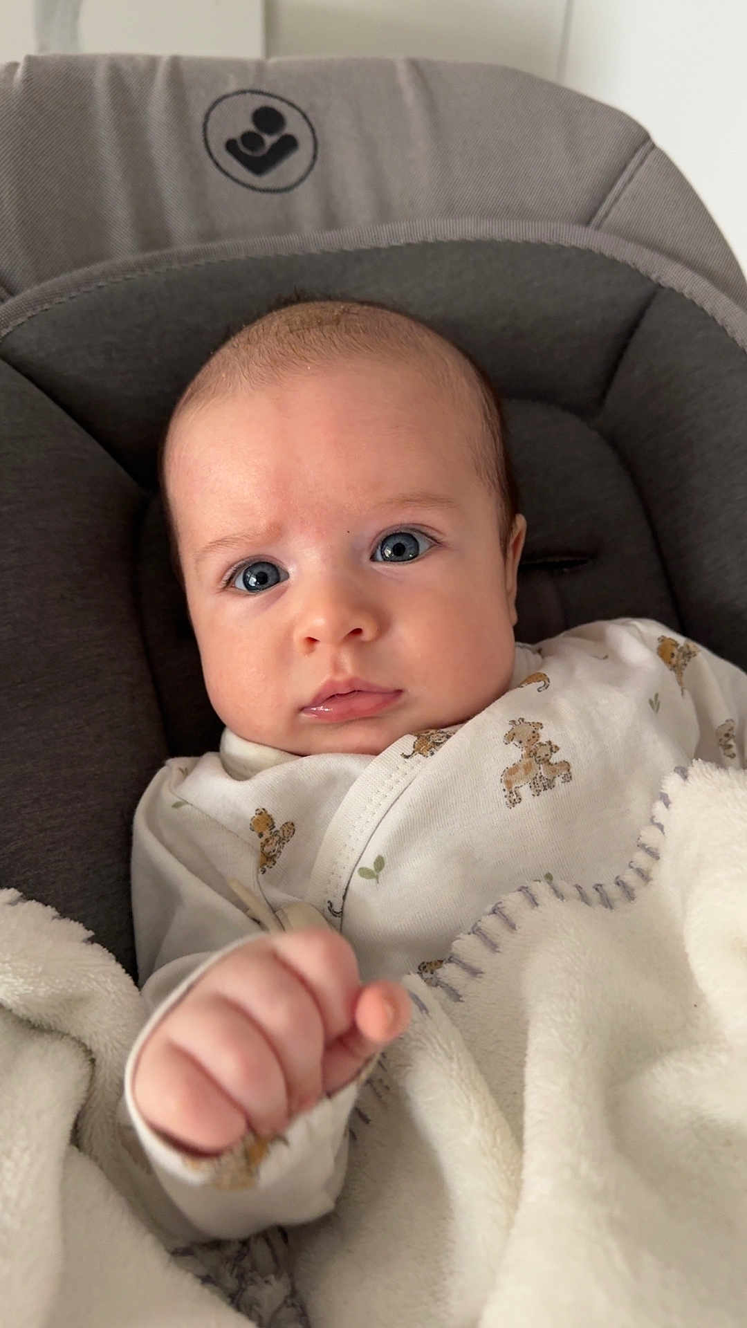 Tiam participe au concours pour gagner de l'argent avec cette photo : baby, infant, blanket, onesie, giraffe_pattern, blue_eyes, cute, cozy, hand, fist, portrait, closeup, indoor, soft, child, young, face, expression, person, seated