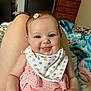 baby, child, smiling, tongue_out, pink_clothing, bib, hair_clip, indoor, person, infant, happy, face, cute, sitting, legs, bedroom, blanket, furniture, soft_lighting, cozy