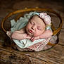baby, newborn, sleeping, headband, flower, basket, blanket, wooden_floor, infant, peaceful, soft_focus, portrait, cute, resting, cozy, pink, delicate, closeup, child, adorable