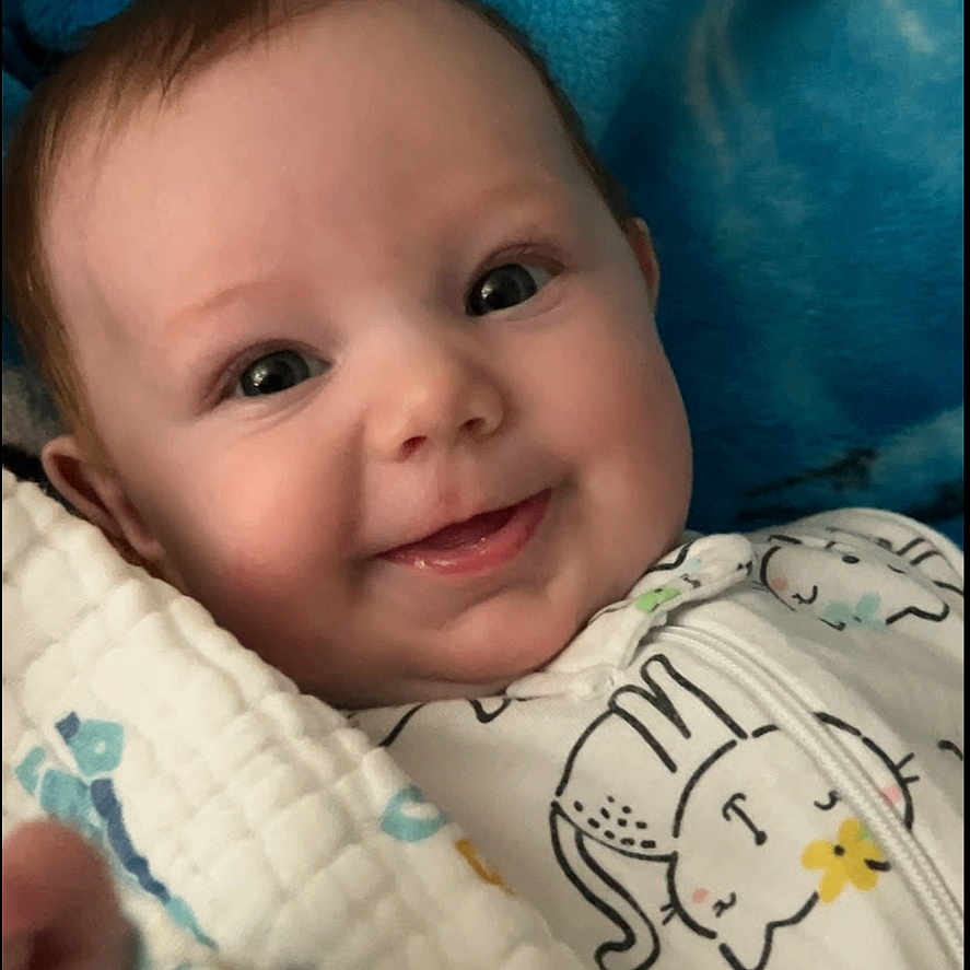 Maddie is registered to the contest to win money with this photo: baby, blanket, blue, cat_print, child, closeup, clothing, comfortable, cozy, cute, face, happy, indoors, infant, lying_down, onesie, portrait, smiling, soft, warm