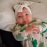 Kaselynn is registered to the contest to win money with this photo: baby, infant, headband, bow, onesie, clothing, pillow, bed, hands, face, cheeks, cute, smiling, indoor, child, sleepwear, green, white, pattern, portrait