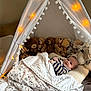 baby, blanket, tent, stuffed_animals, teddy_bear, fairy_lights, soft_toys, cozy, child, indoor, pillow, striped_clothing, sleeping_area, cute, comfort, nursery, decor, warm_lighting, resting, infant