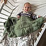 baby, crib, blanket, knitted_blanket, striped_sweater, smiling, infant, bed, sleepwear, wooden_crib, child, happy, indoors, face, person, cute, resting, playful, soft_texture, cozy