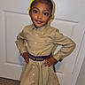 child, girl, portrait, smiling, standing, indoors, door, bow, hair_bow, ponytail, dress, shirt, belt, fashion, outfit, hands_on_hips, brown_hair, earrings, carpet, photography