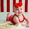 baby, child, red_bow, smile, blue_eyes, blanket, tummy, red_outfit, striped_background, indoor, cute, infant, portrait, happy, face, headband, soft_texture, person, crawling, bright