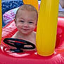 toddler, child, inflatable, pool, water, toy, steering_wheel, red, yellow, summer, smile, face, wet, outdoor, play, fun, baby, cute, expression, skin