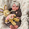 baby, pacifier, headband, plush_toy, bunny, blanket, quilt, floral_pattern, clothing, infant, cute, indoors, child, smiling, foot, hand, soft_toy, portrait, cozy, warm