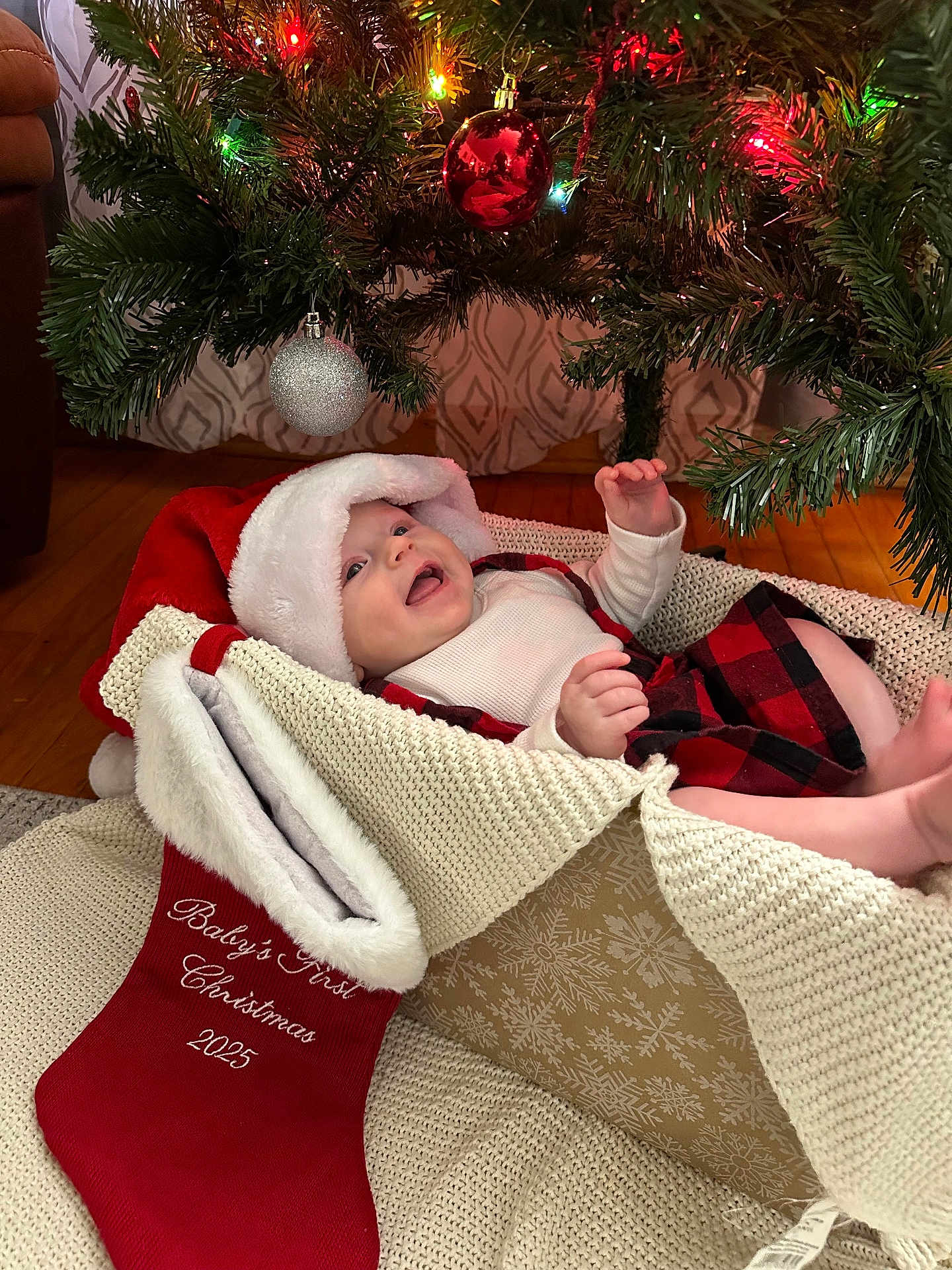Isla joined the competition — help win amazing prizes! baby, christmas_tree, christmas_lights, ornament, stocking, santa_hat, baby_clothing, knitted_basket, holiday, festive, smiling, indoor, floor, wood_floor, curtain, red, white, green, celebration, cute