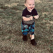 Orion joined the competition — help win amazing prizes! black_shoes, boots, child, daylight, face, grass, greenery, happy, lawn, outdoor, park, patterned_clothing, person, portrait, shorts, smiling, standing, striped_shirt, toddler, toy