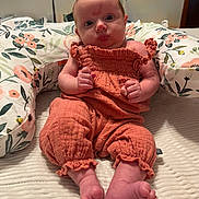 Evelyn is registered to the contest to win money with this photo: baby, infant, child, orange_outfit, bow, pillow, floral_pattern, bed, blanket, feet, hands, indoor, portrait, cute, soft_lighting, person, newborn, clothing, face, sitting