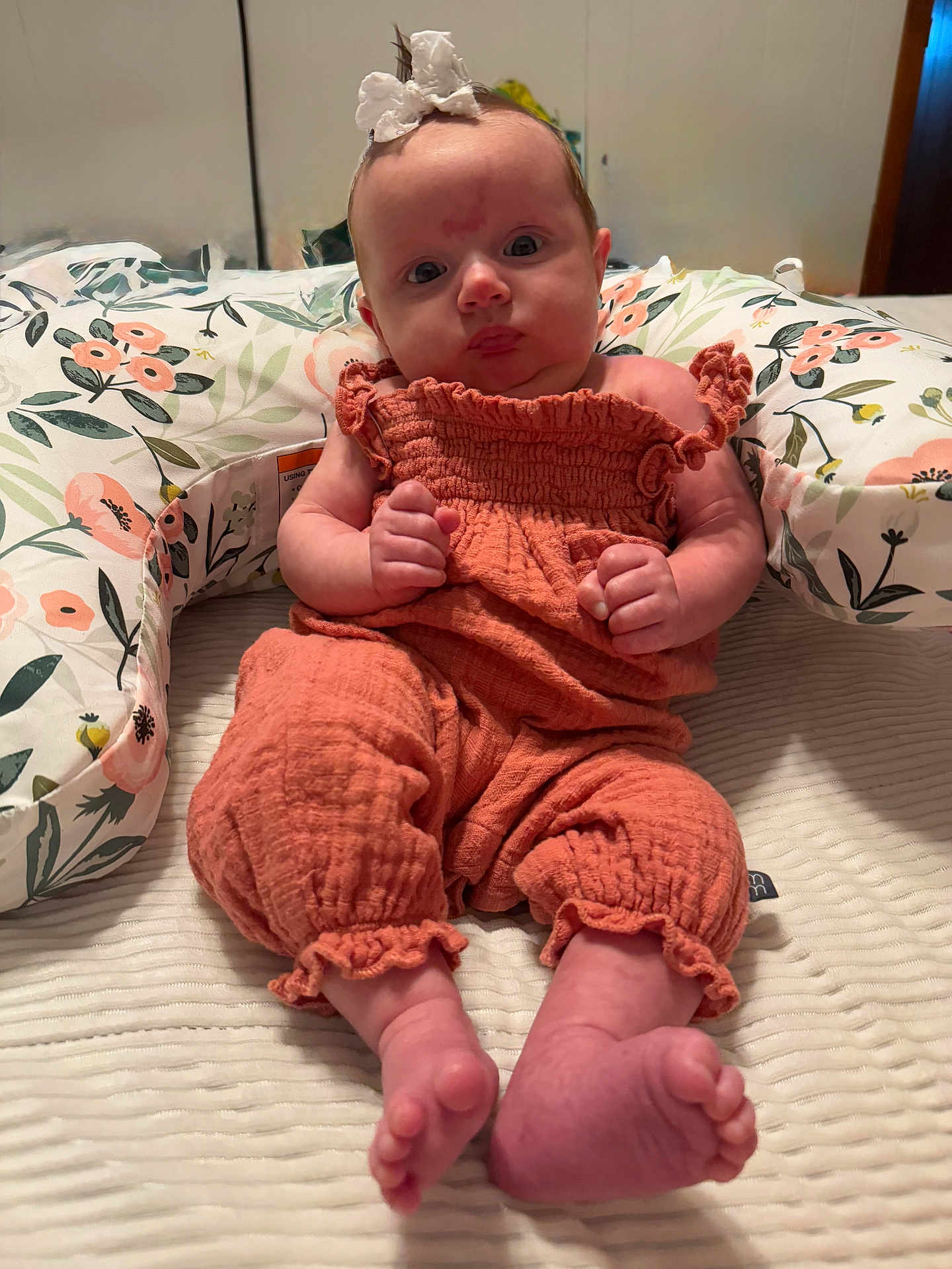 Evelyn is registered to the contest to win money with this photo: baby, infant, child, orange_outfit, bow, pillow, floral_pattern, bed, blanket, feet, hands, indoor, portrait, cute, soft_lighting, person, newborn, clothing, face, sitting