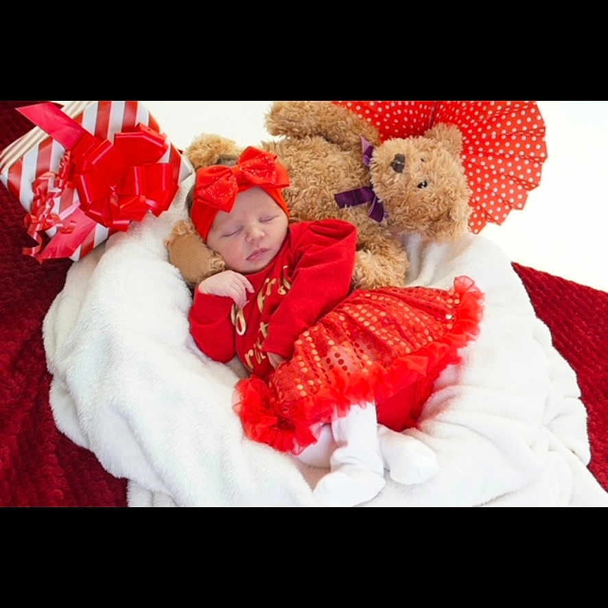 Reneya-Mae joined the competition — help win amazing prizes! adorable, baby, blanket, bow, cozy, cute, festive, gift, headband, holiday, indoors, infant, plush, red_clothing, red_skirt, resting, sleeping, soft_texture, teddy_bear, white_blanket