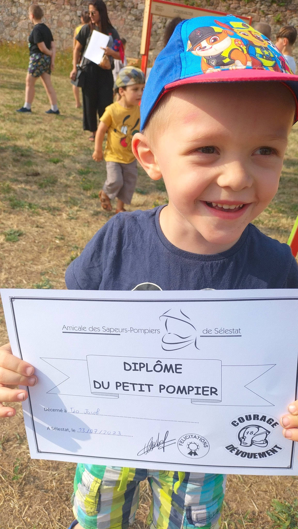 Téo participe au concours pour gagner de l'argent avec cette photo : baseball_cap, blue, cap, cheque, child, face, grass, green, handwriting, happy, headwear, joy, people, person, recreation, red, shorts, smile, snapshot, summer