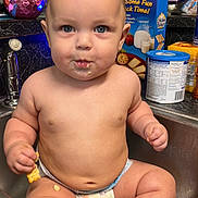Taylen is registered to the contest to win money with this photo: baby, diaper, sink, kitchen, snack, food, crumbs, counter, container, bottle, face, child, curious, wide_eyes, indoor, person, chubby, seated, casual, domestic