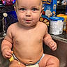 baby, diaper, sink, kitchen, snack, food, crumbs, counter, container, bottle, face, child, curious, wide_eyes, indoor, person, chubby, seated, casual, domestic