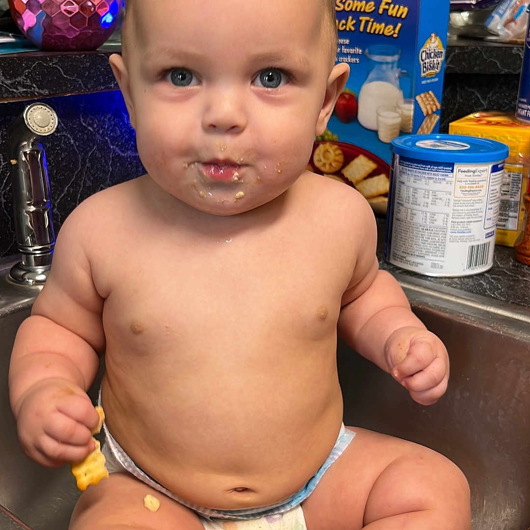 Taylen is registered to the contest to win money with this photo: baby, diaper, sink, kitchen, snack, food, crumbs, counter, container, bottle, face, child, curious, wide_eyes, indoor, person, chubby, seated, casual, domestic