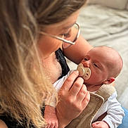 Noham a rejoint le concours — aidez-le/la à gagner de superbes lots ! baby, woman, glasses, pacifier, holding, indoor, closeup, face, hand, caring, love, infant, person, skin, clothing, sleeve, couch, blurred_background, gentle, tender