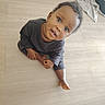 baby, barefoot, blanket, child, clothing, curious, eyes, face, hair, hand, indoor, looking_up, onesie, playful, portrait, sitting, smile, toddler, towel, wooden_floor