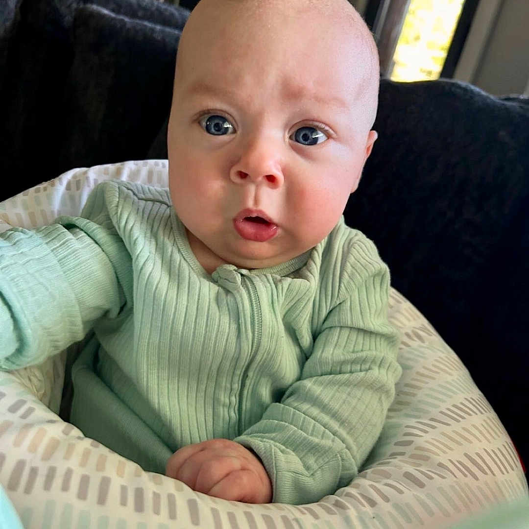 Crew Jensen joined the competition — help win amazing prizes! baby, blue_eyes, child, closeup, curious, cushion, expression, face, furniture, green_clothing, home, indoor, infant, living_room, onesie, person, portrait, sitting, soft_lighting, window