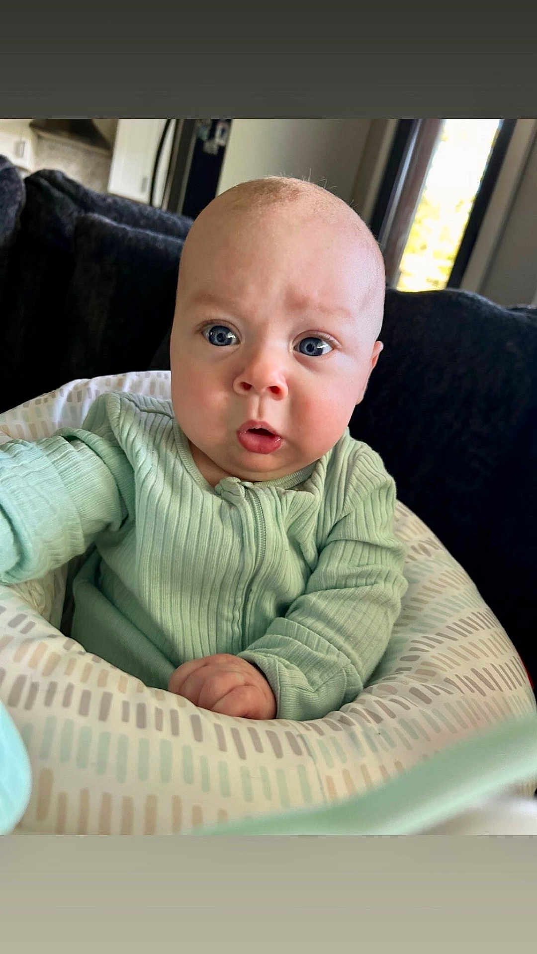 Crew Jensen joined the competition — help win amazing prizes! baby, infant, child, onesie, green_clothing, cushion, face, blue_eyes, indoor, window, furniture, living_room, expression, curious, portrait, sitting, closeup, person, home, soft_lighting