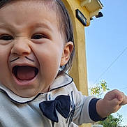 Sebastian is registered to the contest to win money with this photo: toddler, child, face, expression, smile, mustache, clothing, bow_tie, outdoor, sky, building, yellow_wall, hand, happy, cute, portrait, person, funny_face, baby, daylight