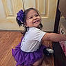 Layla joined the competition — help win amazing prizes! child, girl, toddler, smiling, happy, portrait, indoor, purple, tutu, dress, hair_bow, flower, long_hair, reaching, sitting, wooden_floor, door, table, candid, playful
