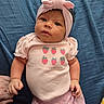 baby, infant, pink_clothing, headband, bow, strawberry_print, hand_holding, blue_blanket, cute, portrait, child, newborn, soft_fabric, lying_down, curious_expression, skin, face, person, indoor, toddler